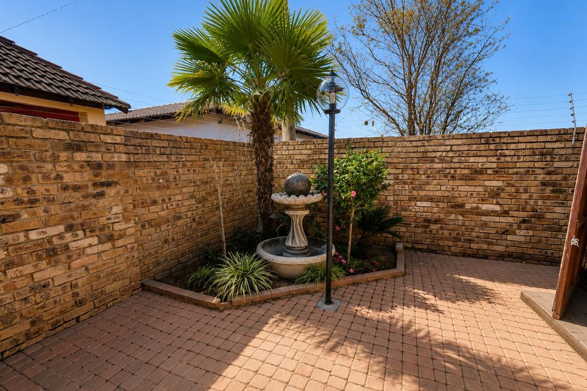 A private rear courtyard featuring brick boundary walls, paved flooring, a central water feature, and established garden landscaping.