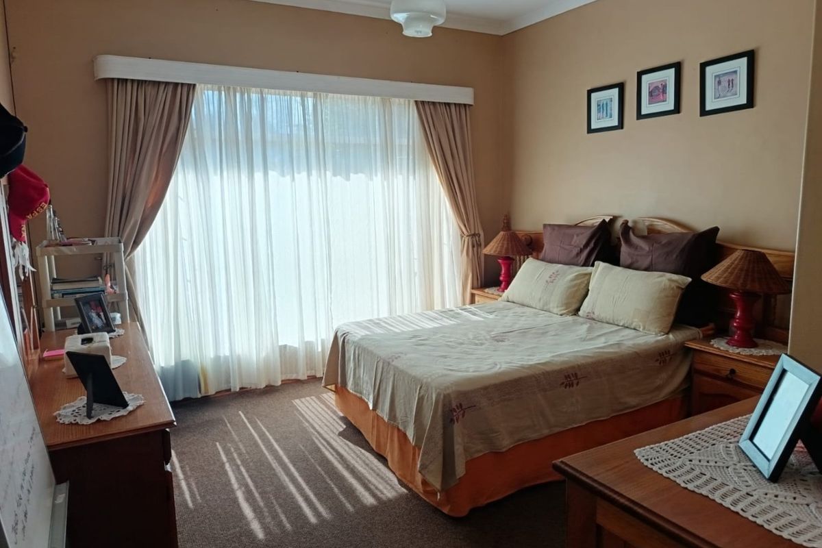 A carpeted bedroom featuring large windows with curtain tracks and a central ceiling light fixture, offering a functional and lived-in space.