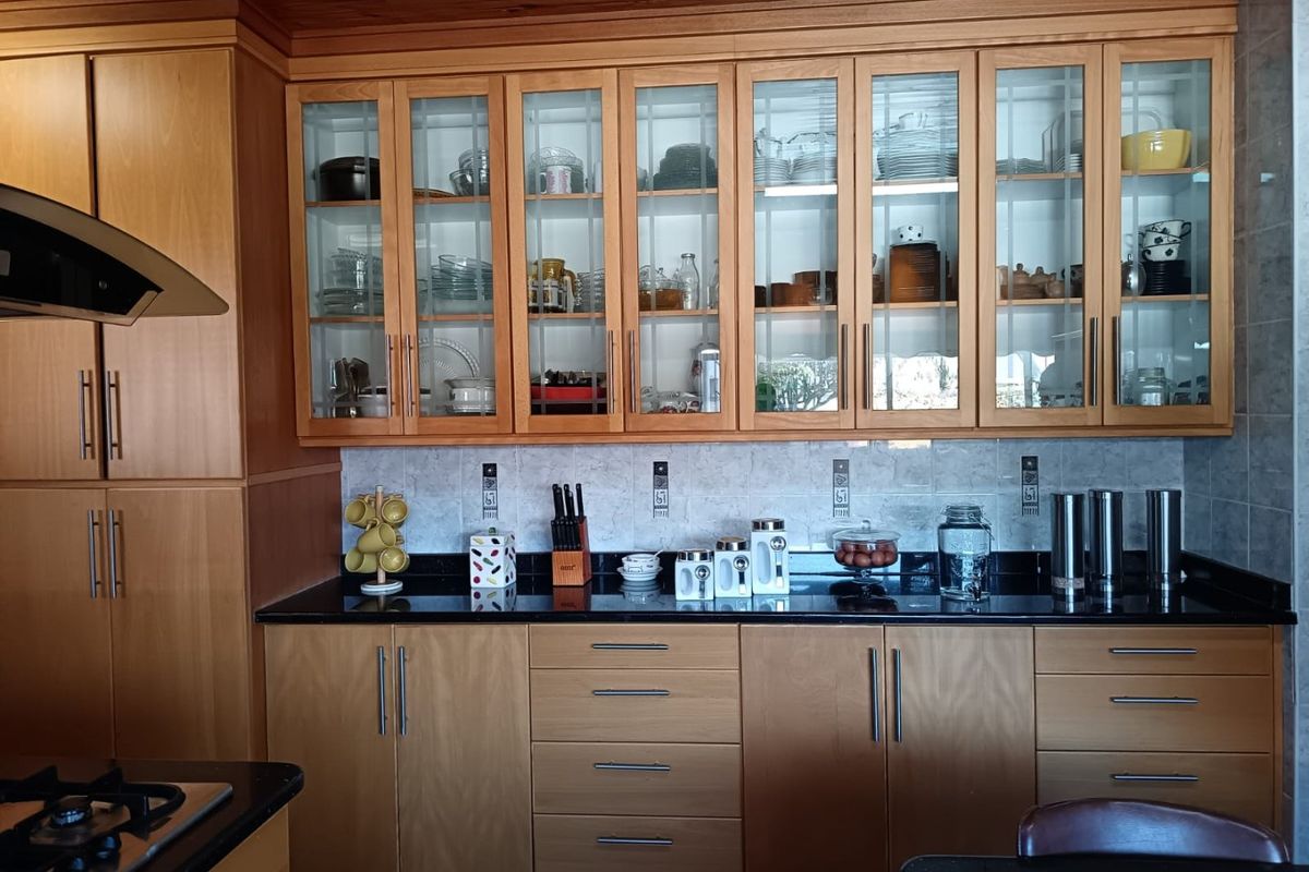 A well-maintained kitchen featuring warm timber cabinetry, glass-fronted display cupboards, black granite countertops, and a tiled backsplash with a built-in gas hob.