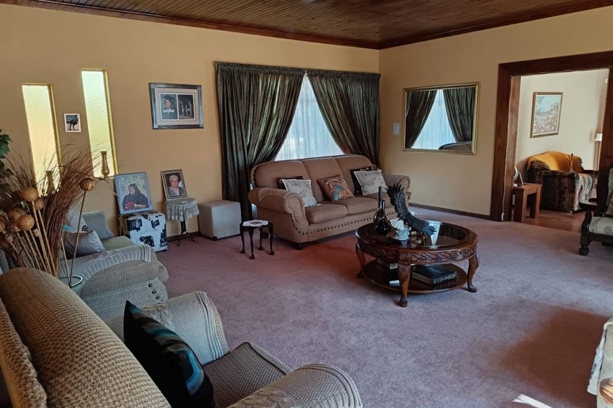 A spacious living room featuring a traditional timber-paneled ceiling, carpeted flooring, and a wide doorway leading to an adjacent room.