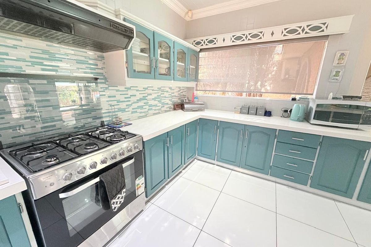 A well-maintained kitchen featuring blue cabinetry, stone countertops, a gas stove with extractor fan, and modern tiled flooring.