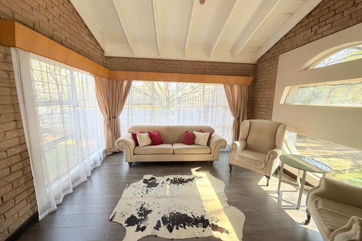 A bright living room featuring exposed brick walls, high exposed beam ceilings, and large windows that provide ample natural light.