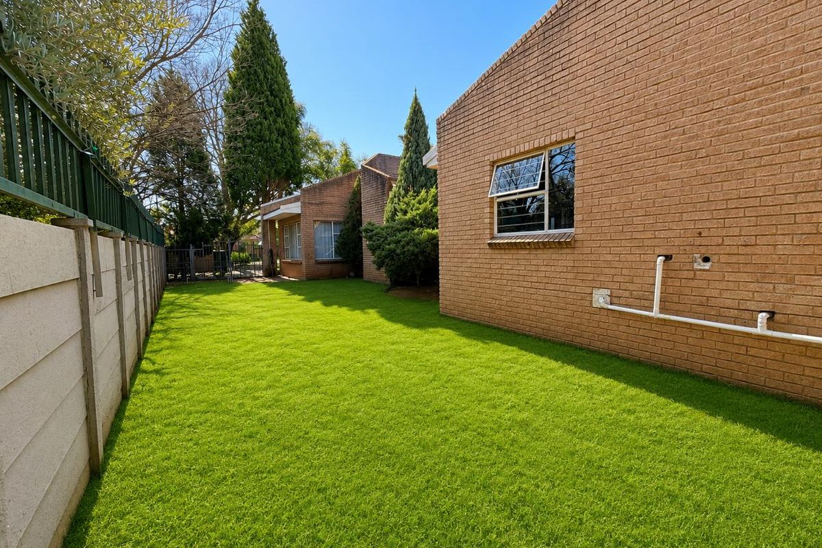A well-maintained rear garden area featuring a neat lawn, face brick exterior walls, and secure boundary fencing.