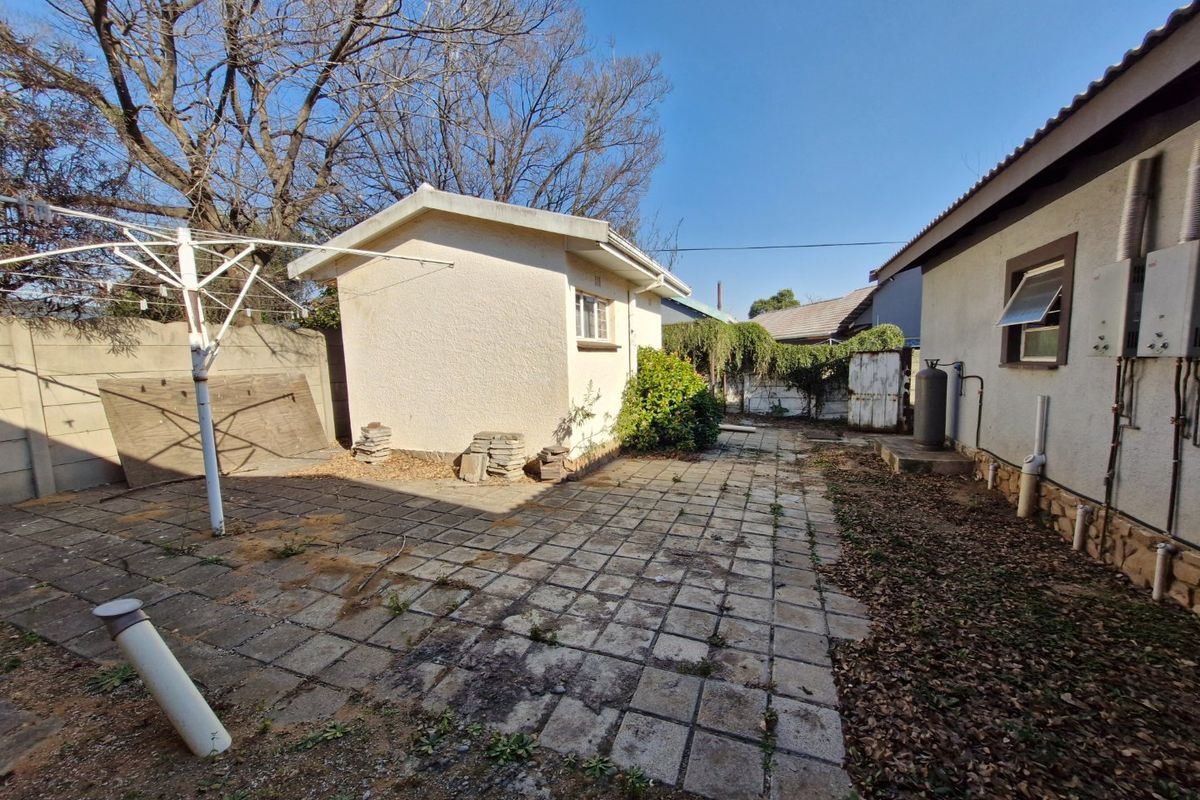 Rear exterior area featuring a paved patio, an outbuilding, and boundary walling, requiring maintenance and landscaping to improve the outdoor space.