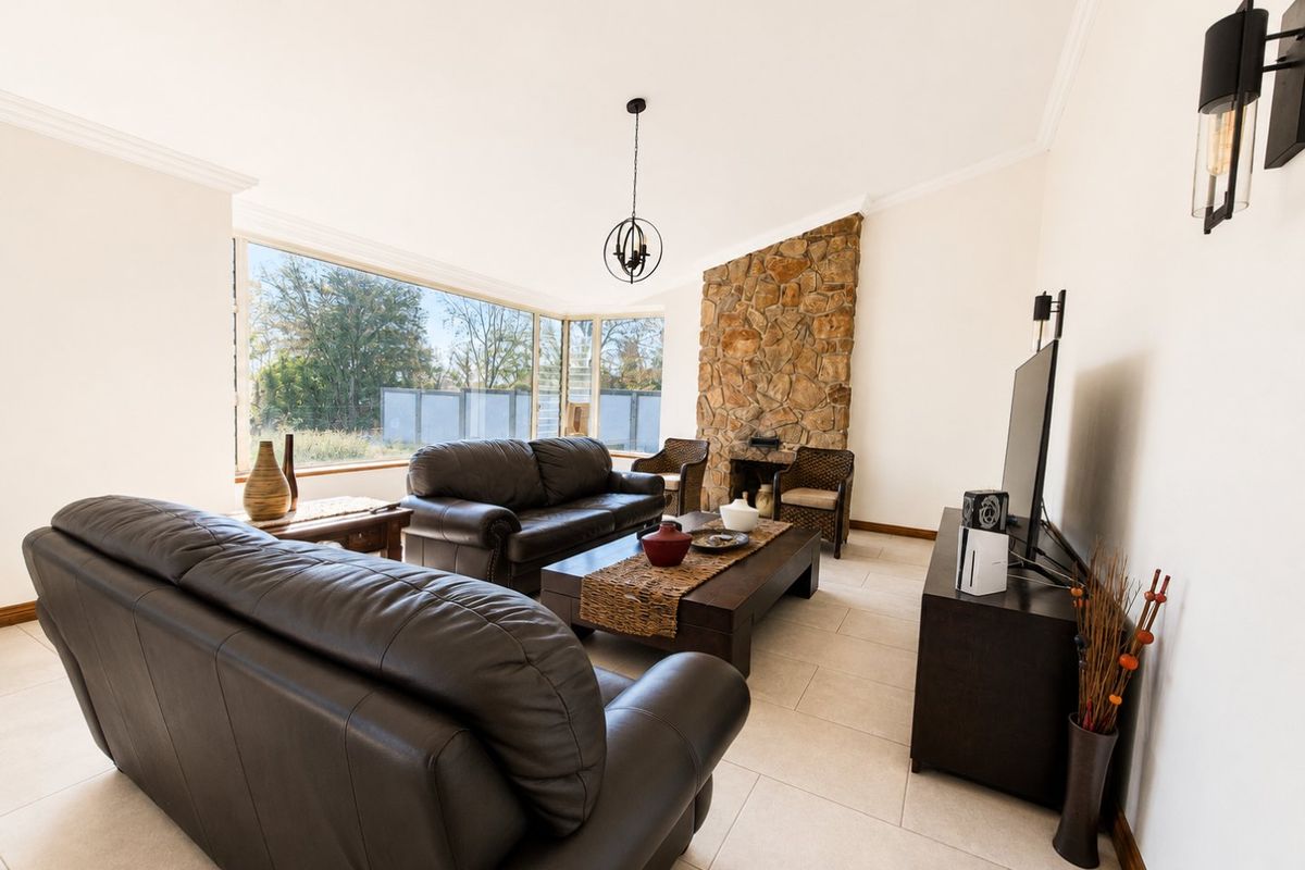 A bright living room featuring a prominent stone fireplace, large picture windows providing natural light, and neutral tiled flooring.