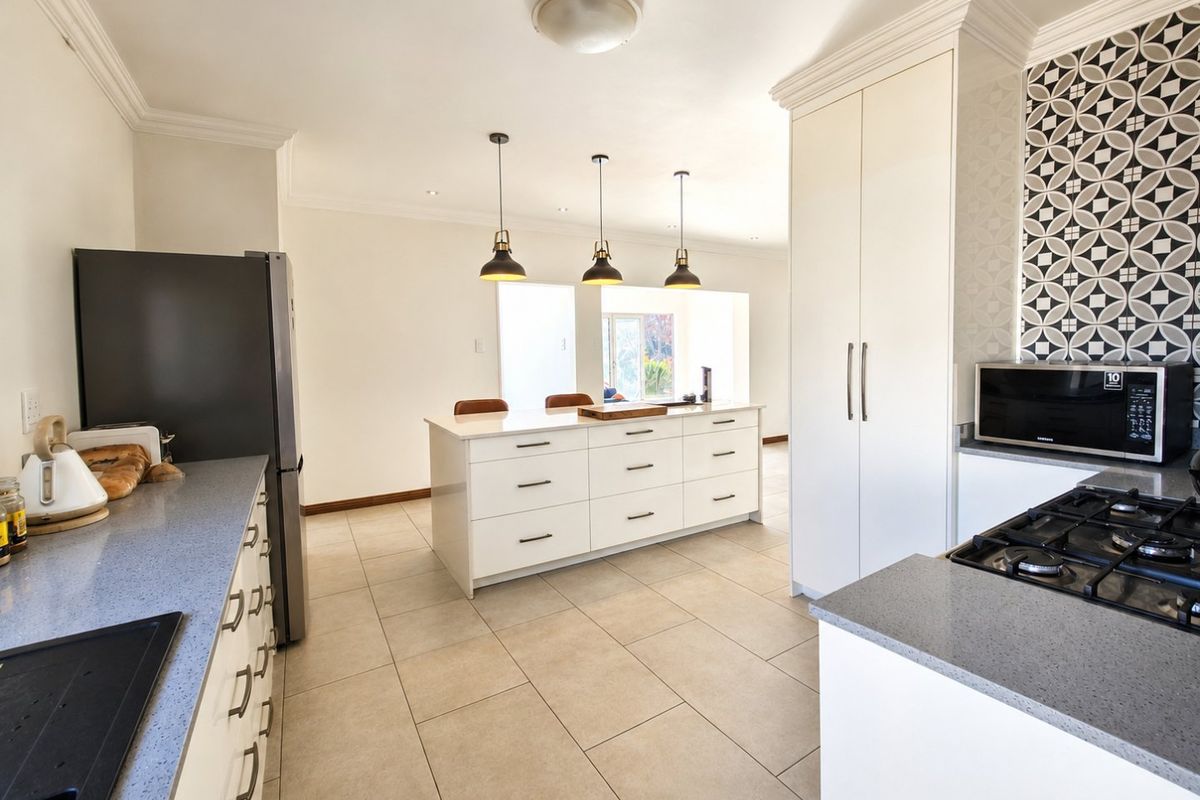 Modern kitchen featuring a central island, stone countertops, gas cooktop, and stylish decorative backsplash with ample built-in storage.