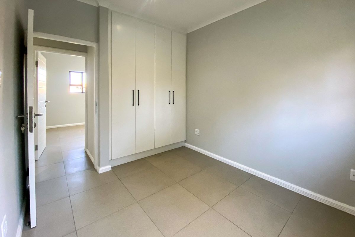 A clean, empty bedroom featuring neutral grey walls, large format floor tiles, and modern white built-in cupboards.