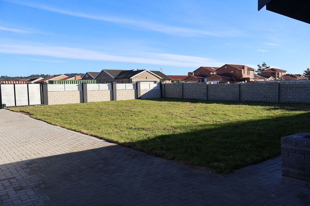 A spacious rear garden featuring a large lawn area, paved driveway, and secure concrete block boundary walls.