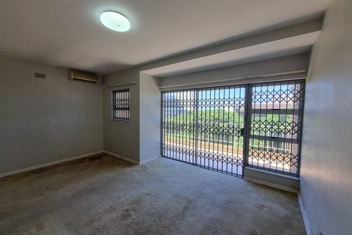 An empty living room featuring carpet flooring, an air conditioning unit, and large sliding glass doors with security gates leading to an outdoor area.