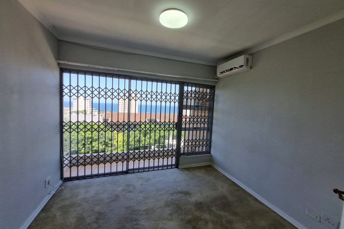 An empty bedroom featuring a split-system air conditioner, carpeted flooring, and a sliding glass door with a security gate leading to a balcony.