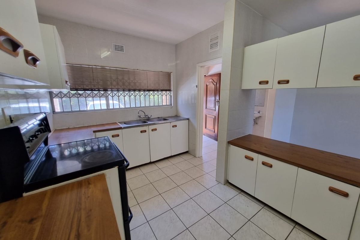 A functional kitchen featuring tiled flooring, built-in cabinetry with wooden countertops, and a double basin sink, offering a clean and practical workspace.