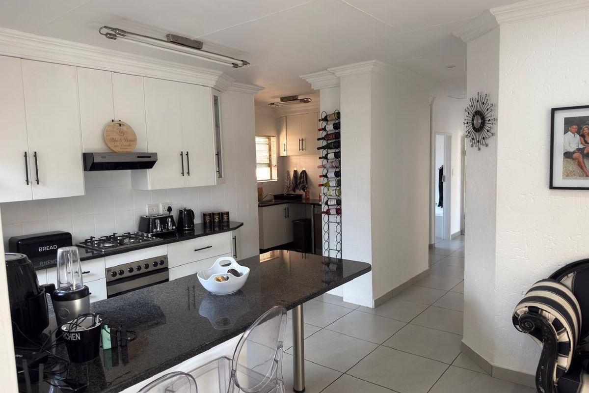 Modern kitchen featuring white cabinetry, granite countertops, a gas hob, and a breakfast bar, with an adjacent scullery area and tiled flooring.