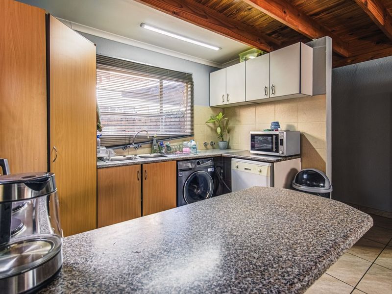 Functional kitchen featuring granite countertops, laminate cabinetry, tiled backsplash, and exposed timber ceiling beams, with integrated laundry plumbing and tiled flooring.