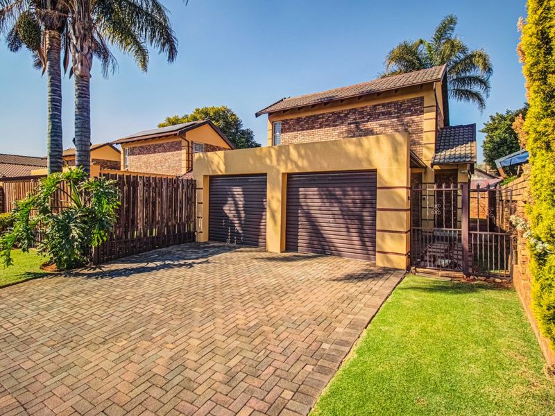 Front view of a residential property featuring a double garage, paved driveway, and established garden area.