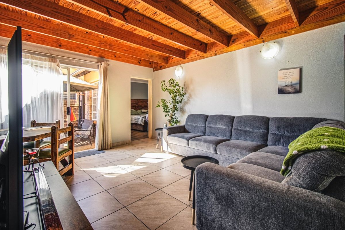 A comfortable living room featuring exposed timber beam ceilings, ceramic tiled flooring, and direct access to an outdoor patio area.