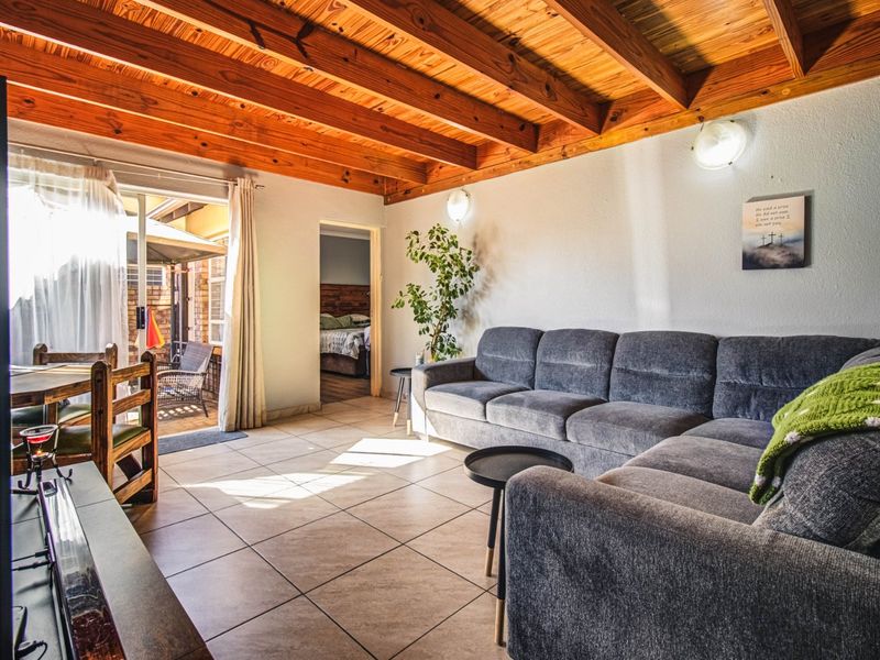 A comfortable living room featuring exposed timber beam ceilings, ceramic tiled flooring, and direct access to an outdoor patio area.
