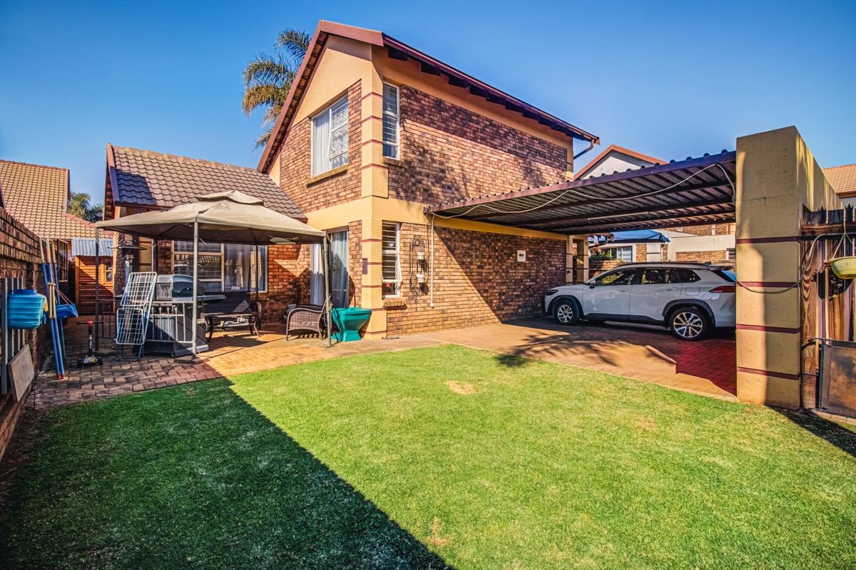 Rear view of the property featuring a brick facade, a covered carport, paved driveway area, and a well-maintained lawn.