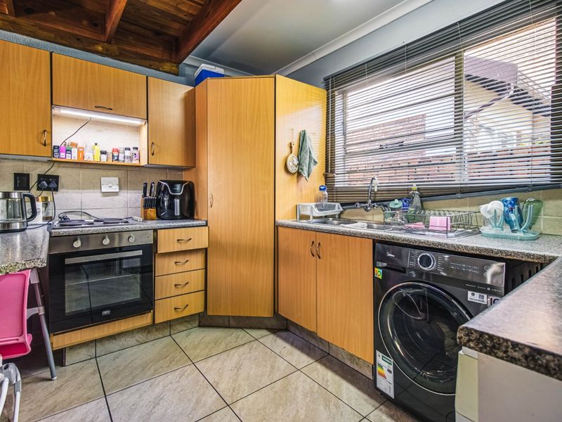 Functional kitchen featuring laminate cabinetry, granite countertops, built-in oven, hob, and exposed timber ceiling beams, providing a practical workspace with tiled flooring.