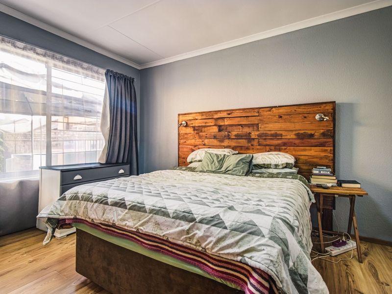 A well-lit bedroom featuring laminate flooring and a custom wooden headboard, offering a comfortable and functional sleeping space.