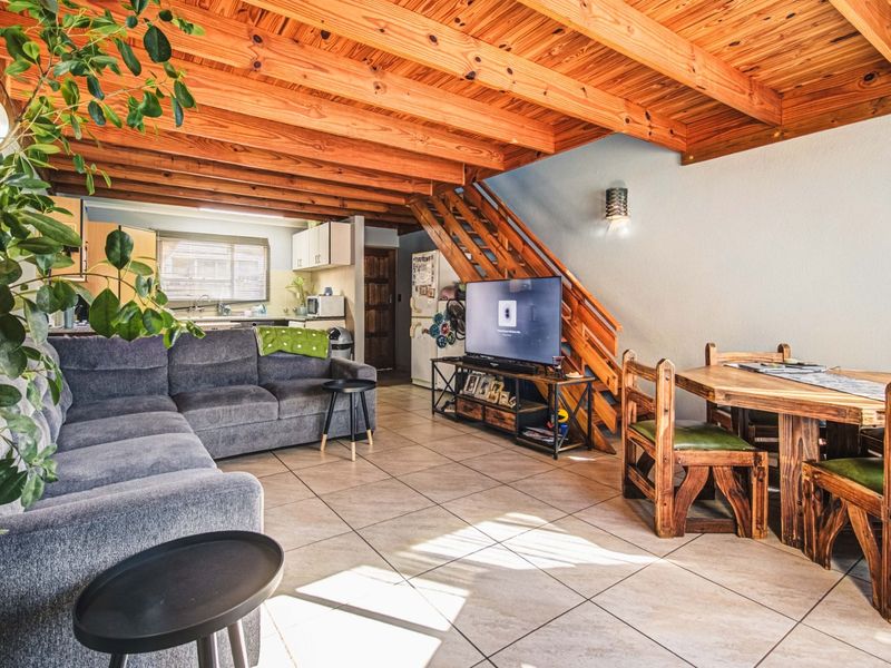 Open-plan living and dining area featuring exposed timber ceiling beams, ceramic tiled flooring, and an integrated kitchen space with a timber staircase.