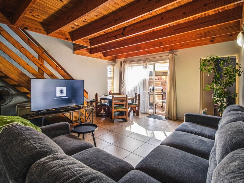 Open-plan living area featuring exposed timber ceiling beams, tiled flooring, and a sliding glass door providing access to the outdoor patio.