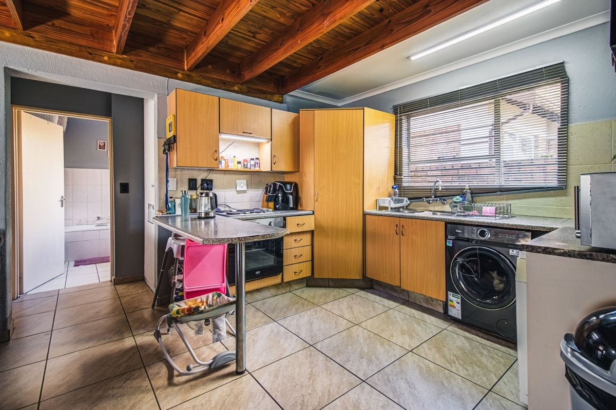 Functional kitchen featuring laminate cabinetry, granite countertops, built-in oven, hob, and exposed timber ceiling beams, with direct access to an adjacent bathroom.