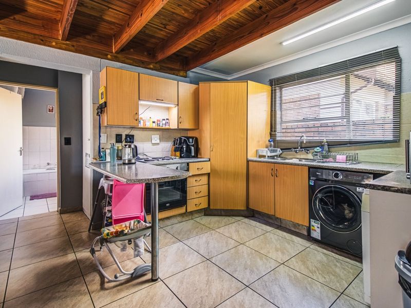 Functional kitchen featuring laminate cabinetry, granite countertops, built-in oven, hob, and exposed timber ceiling beams, with direct access to an adjacent bathroom.