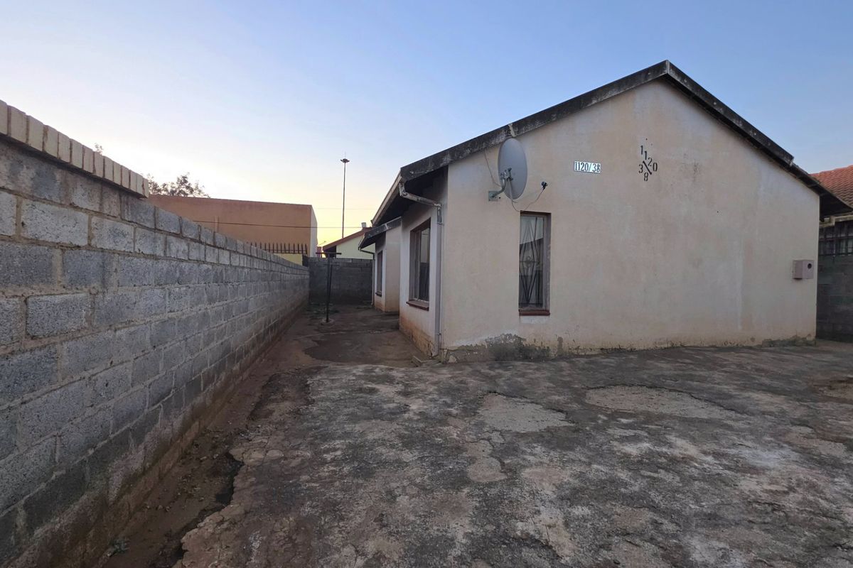 Rear exterior view of the property featuring a concrete boundary wall and paved yard area with visible wear and tear on the surfaces.