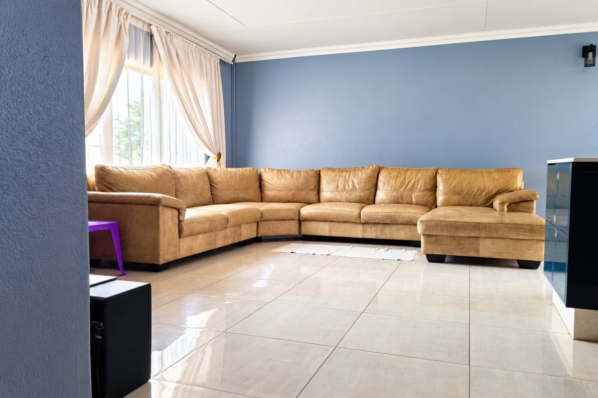 A spacious living room featuring large format floor tiles, blue accent walls, and classic ceiling cornicing, providing a bright and open living area.