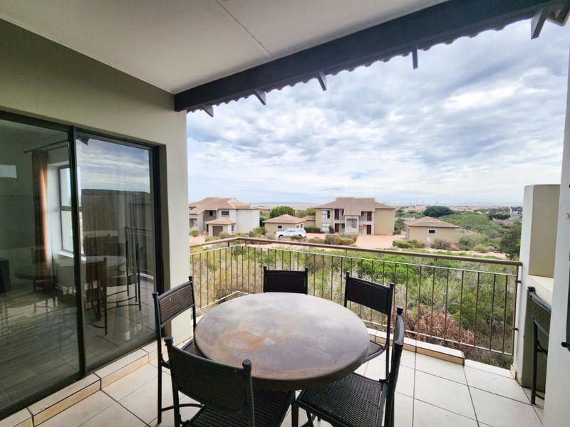 A covered balcony featuring tiled flooring and a metal balustrade, offering an elevated view of the surrounding residential complex.