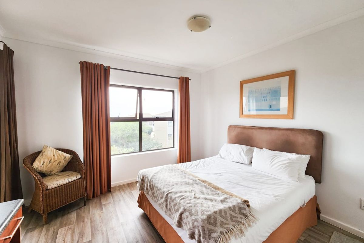 A well-lit bedroom featuring modern laminate flooring, neutral walls, and a large window providing natural light.