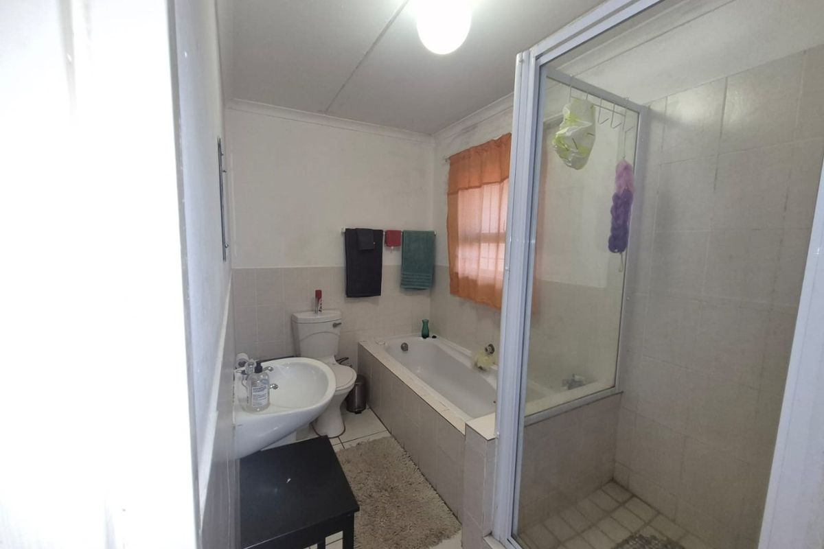 A functional bathroom featuring a bathtub, separate shower enclosure, pedestal basin, and toilet with neutral wall and floor tiling.
