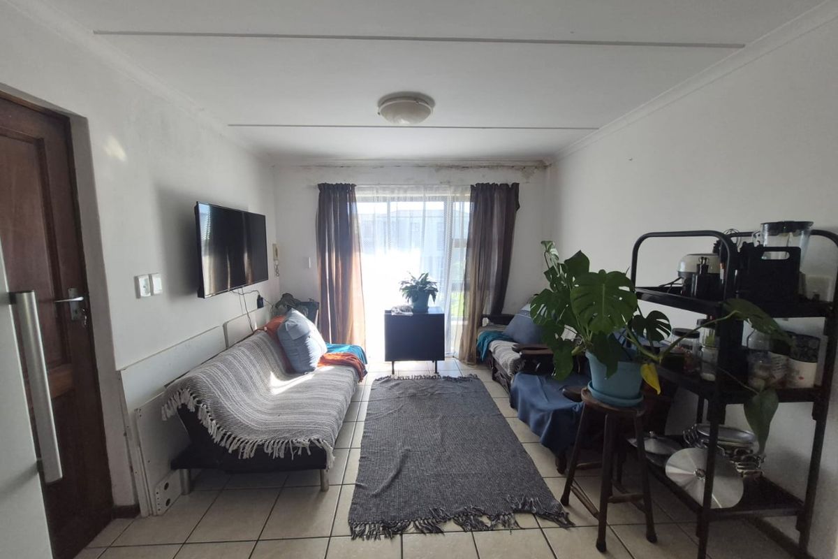A living room featuring tiled flooring and a sliding glass door, showing signs of ceiling water damage and wall wear requiring maintenance.