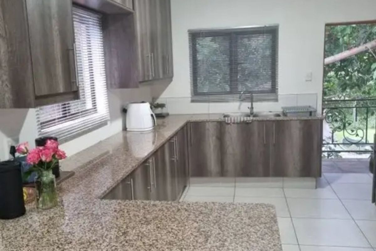 A functional kitchen featuring granite countertops, ample laminated cabinetry, and tiled flooring, with direct access to an outdoor balcony area.