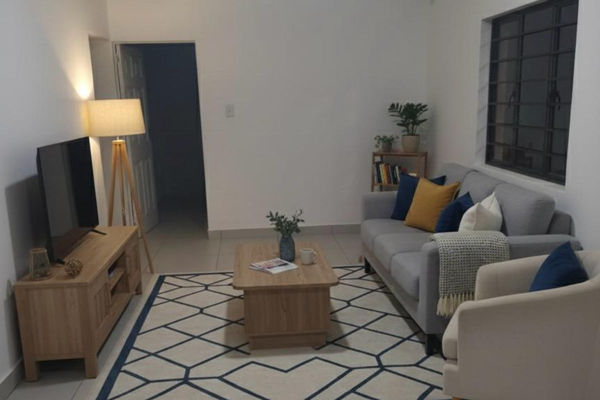 A well-maintained living room featuring neutral tiled flooring, a window with security bars, and clean white walls.
