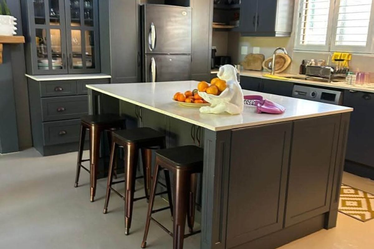 A modern kitchen featuring dark grey cabinetry, a central island with stone countertops, pendant lighting, and integrated storage solutions.