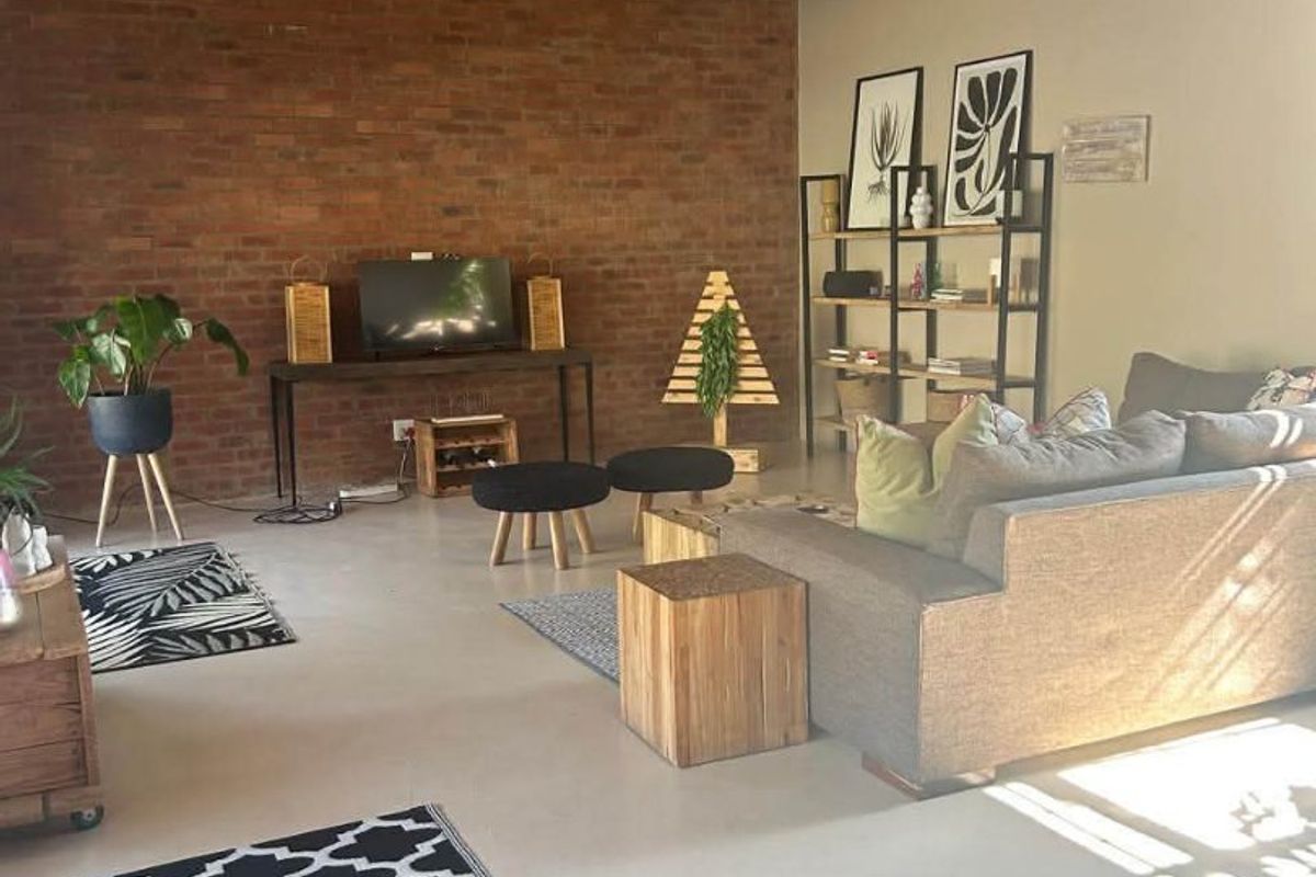 Spacious living area featuring a double-volume vaulted ceiling with exposed timber beams, a prominent exposed brick feature wall, and polished concrete flooring.