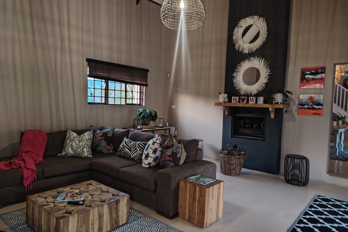 A cozy living room featuring a vaulted ceiling with exposed rafters, a central fireplace with a timber mantelpiece, and neutral tiled flooring.