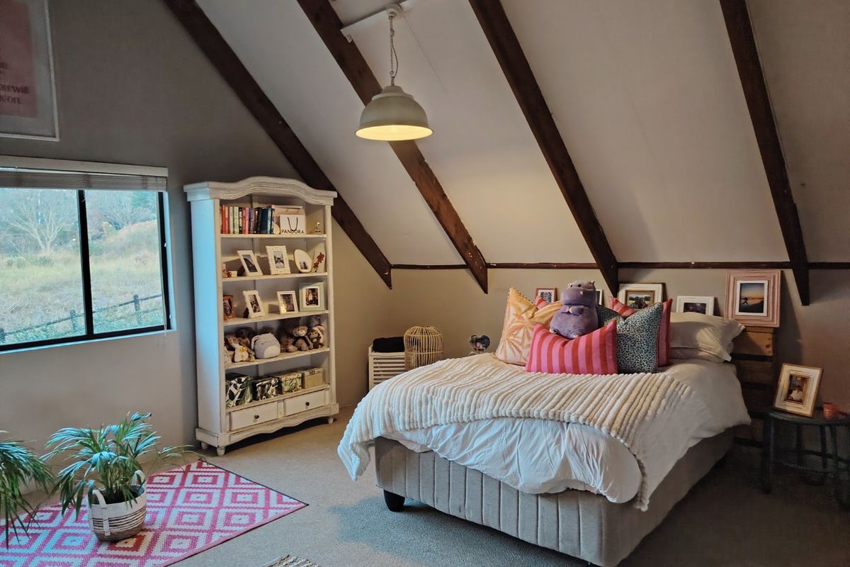A cozy bedroom featuring a vaulted ceiling with exposed timber rafters, neutral walls, and a large window providing natural light and rural views.