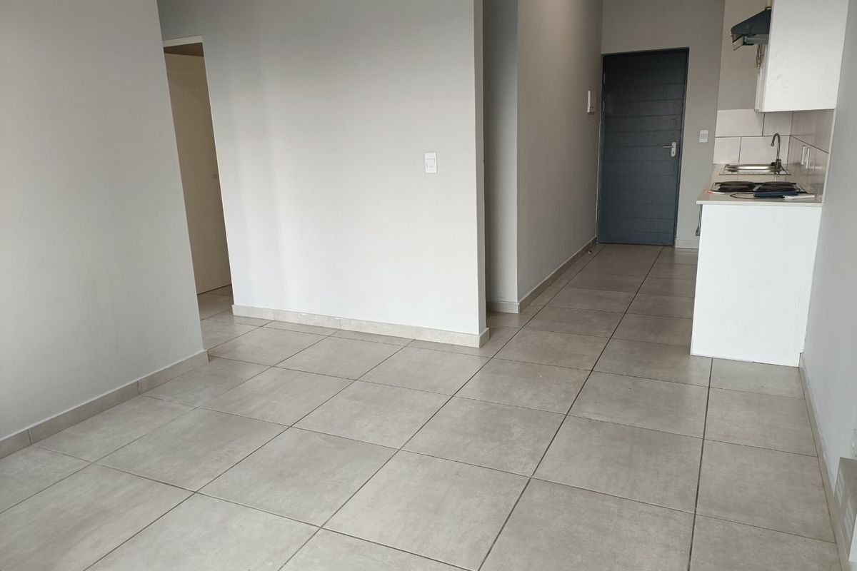 An open-plan living area featuring neutral tiled flooring, a compact kitchen with built-in cabinetry, a sink, and an extractor fan.