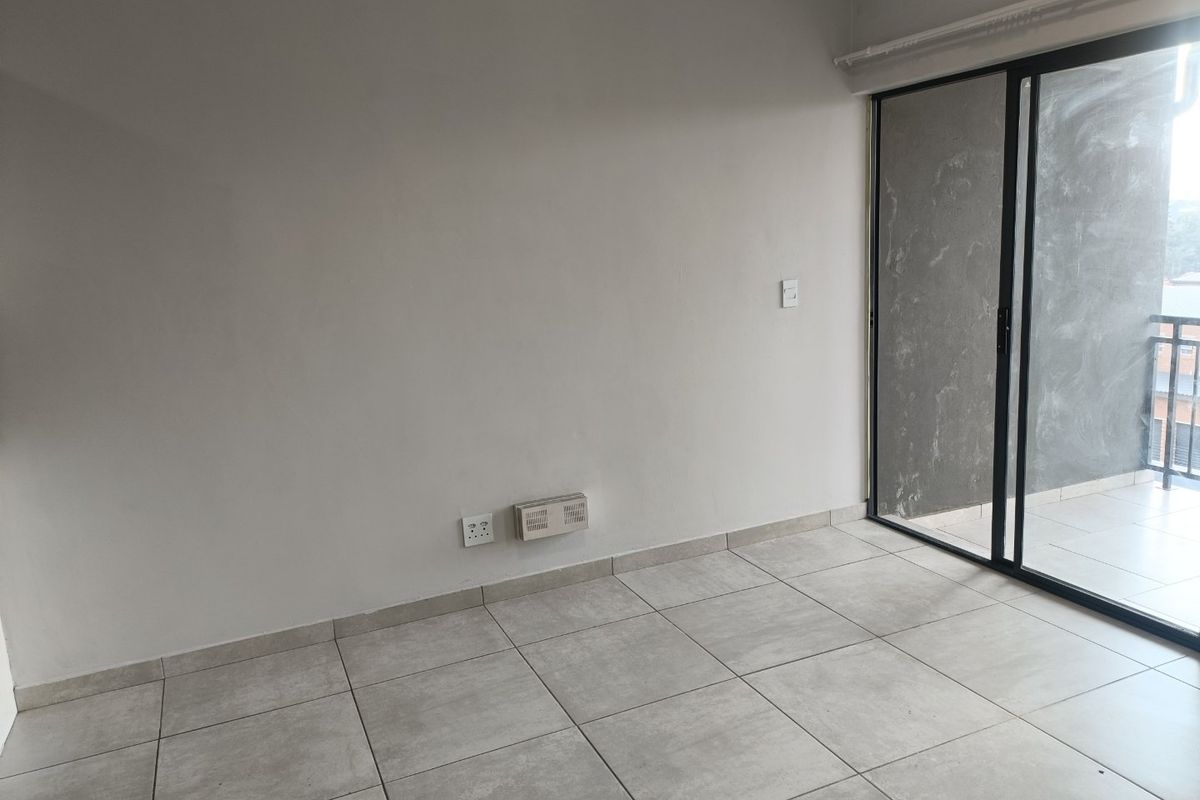 An empty living room featuring neutral tiled flooring and a large sliding glass door providing access to an outdoor balcony area.