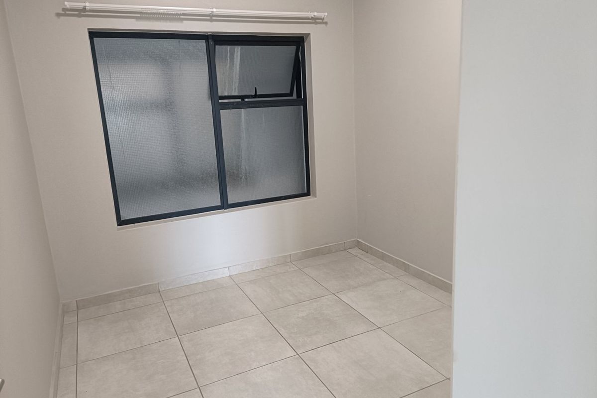 A clean, empty bedroom featuring neutral tiled flooring and an aluminium-framed window with a fitted curtain rail.