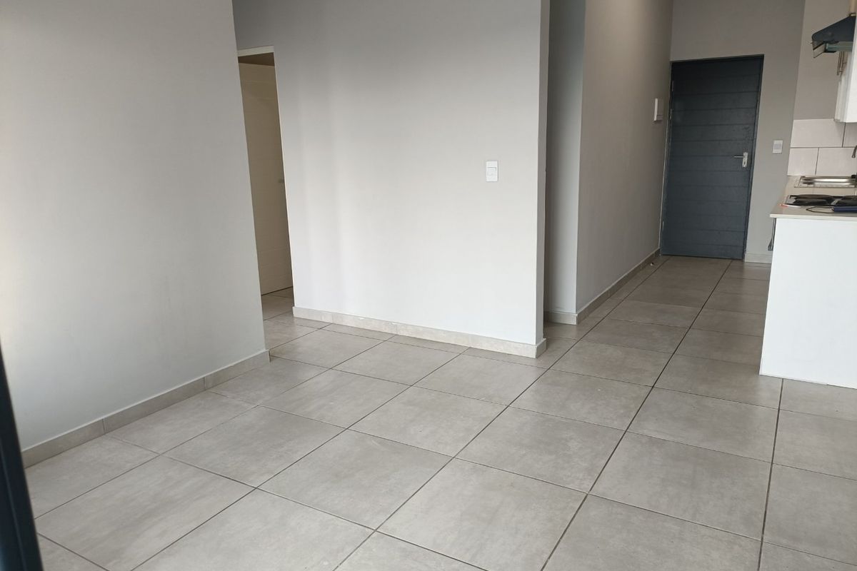 An open-plan living area featuring neutral tiled flooring and a compact kitchen corner with built-in cabinetry and integrated appliances.