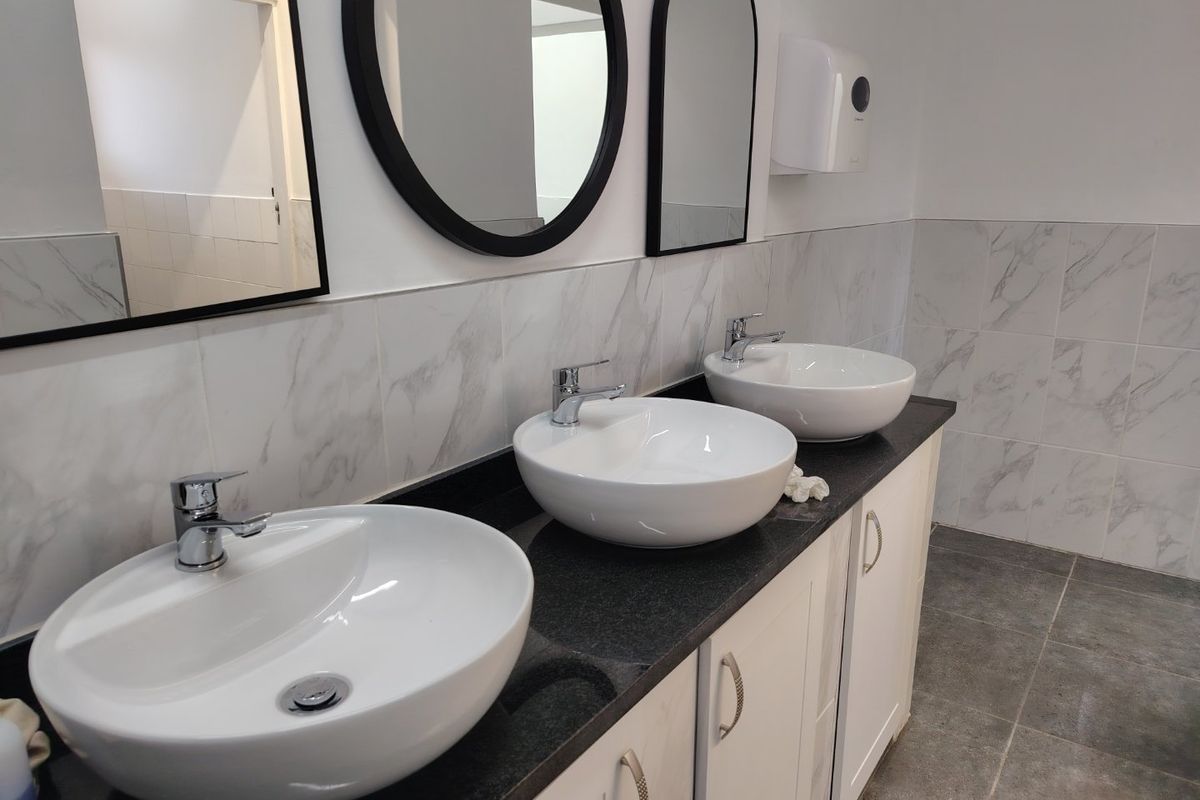 Modern commercial bathroom featuring a triple vanity with vessel sinks, chrome mixer taps, marble-look wall tiling, and wall-mounted mirrors.