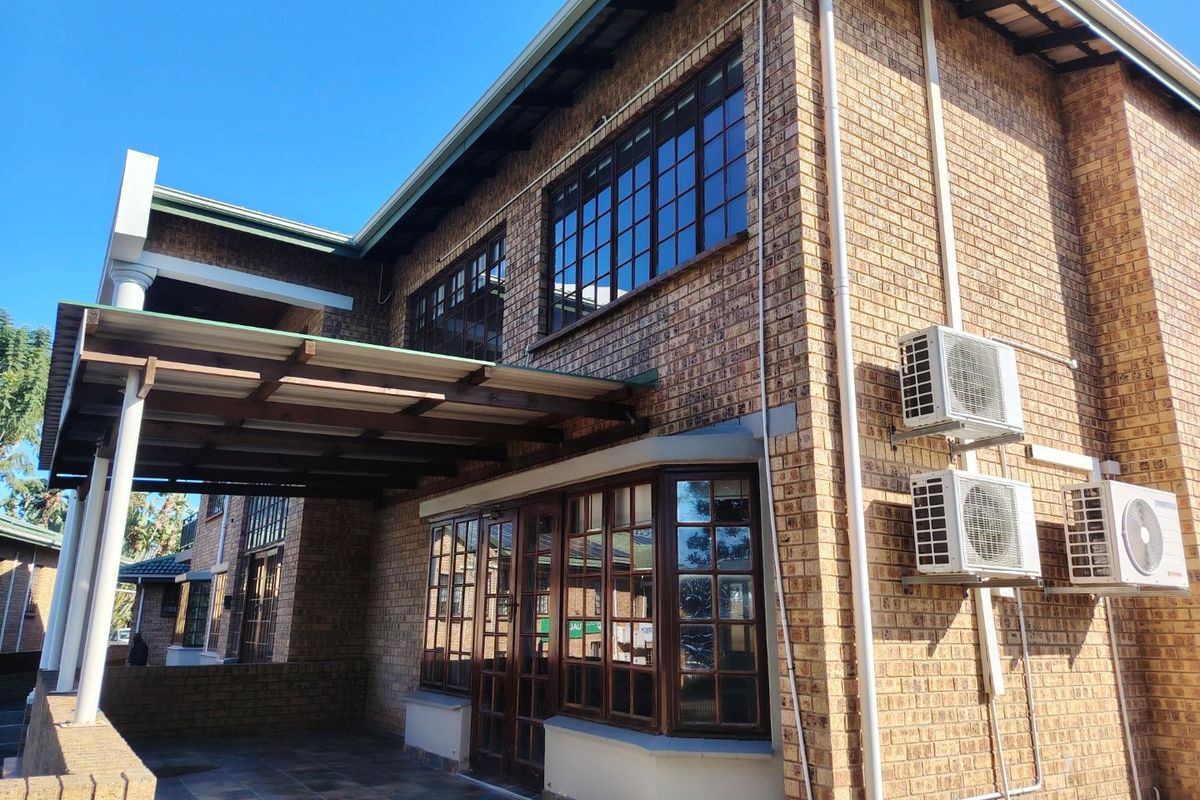 A view of the rear exterior featuring a face brick facade, timber framed windows, and a covered patio area with mounted air conditioning units.
