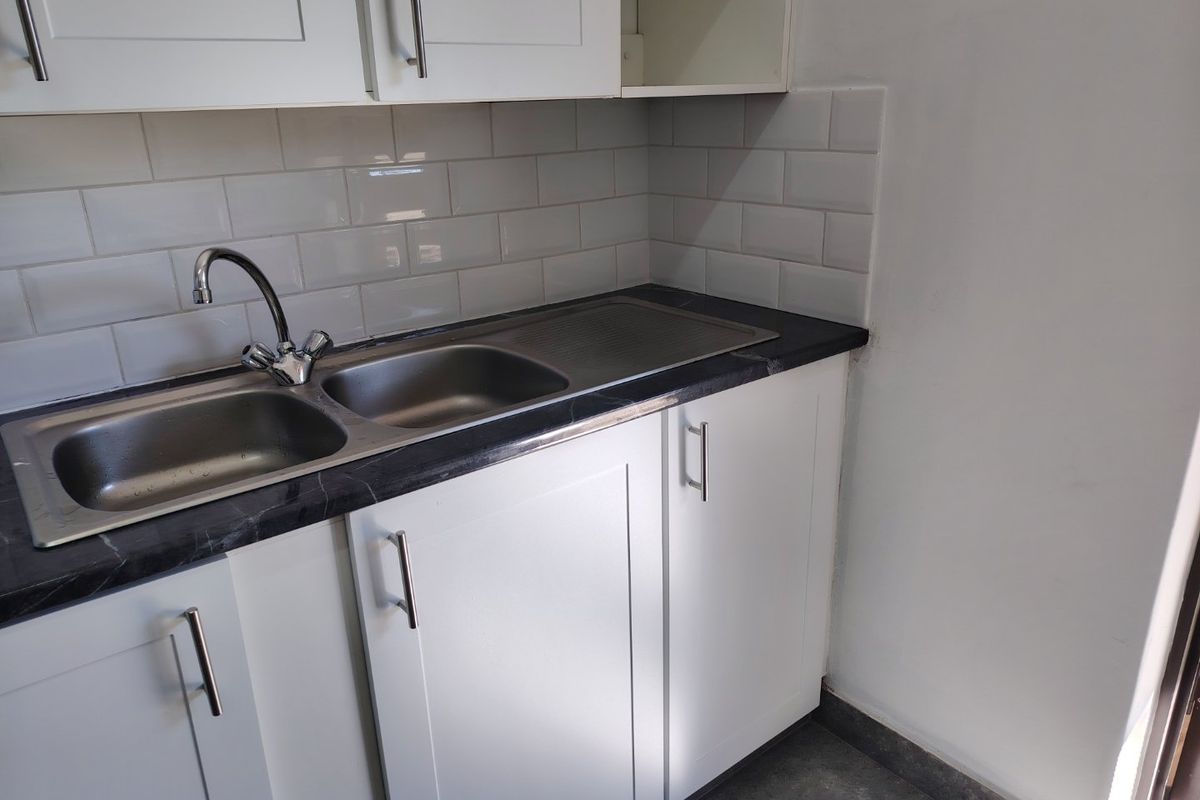 A clean, functional kitchen kitchenette area featuring white cabinetry, a stainless steel sink, and a modern subway tile backsplash.