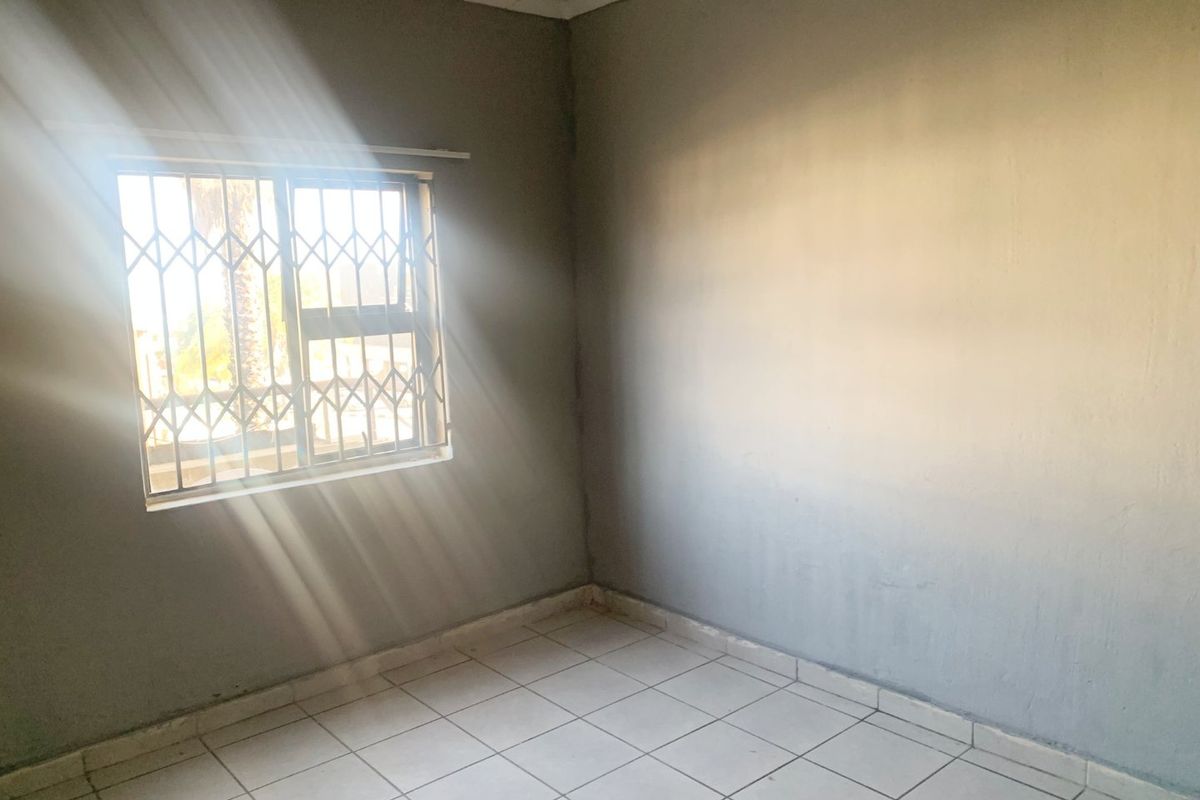 An empty bedroom featuring tiled flooring and a window fitted with a security gate, offering a blank canvas for potential interior design updates.