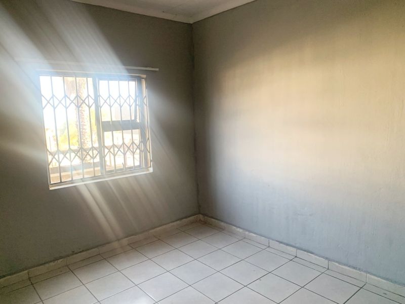 An empty bedroom featuring tiled flooring and a window fitted with a security gate, offering a blank canvas for potential interior design updates.