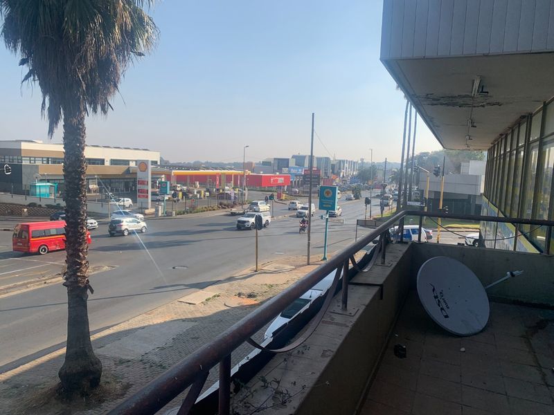 An elevated balcony overlooking a busy street intersection, featuring a metal railing and tiled flooring with visible signs of wear and weathering.
