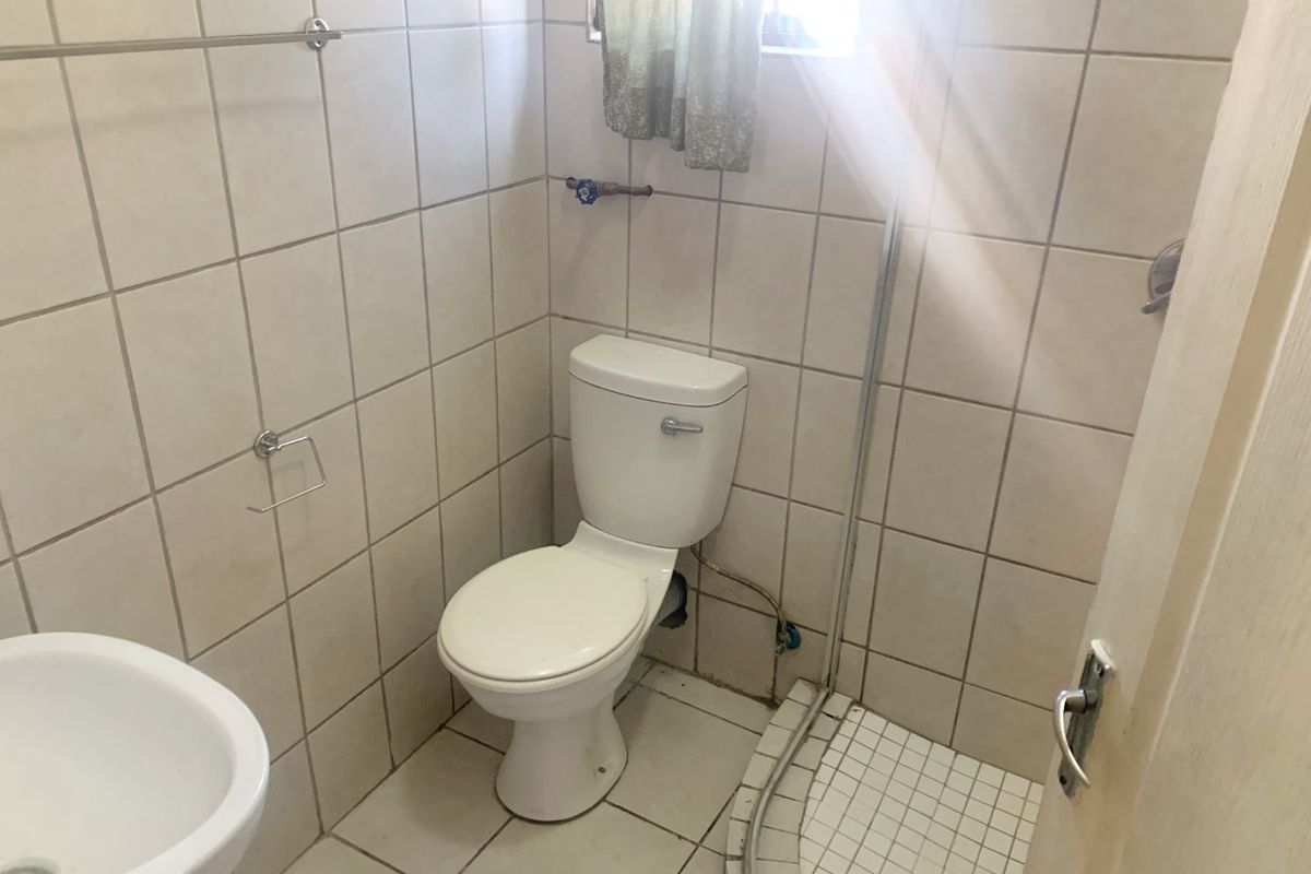 A compact bathroom featuring a toilet, shower cubicle, and washbasin with neutral ceramic tiling throughout.